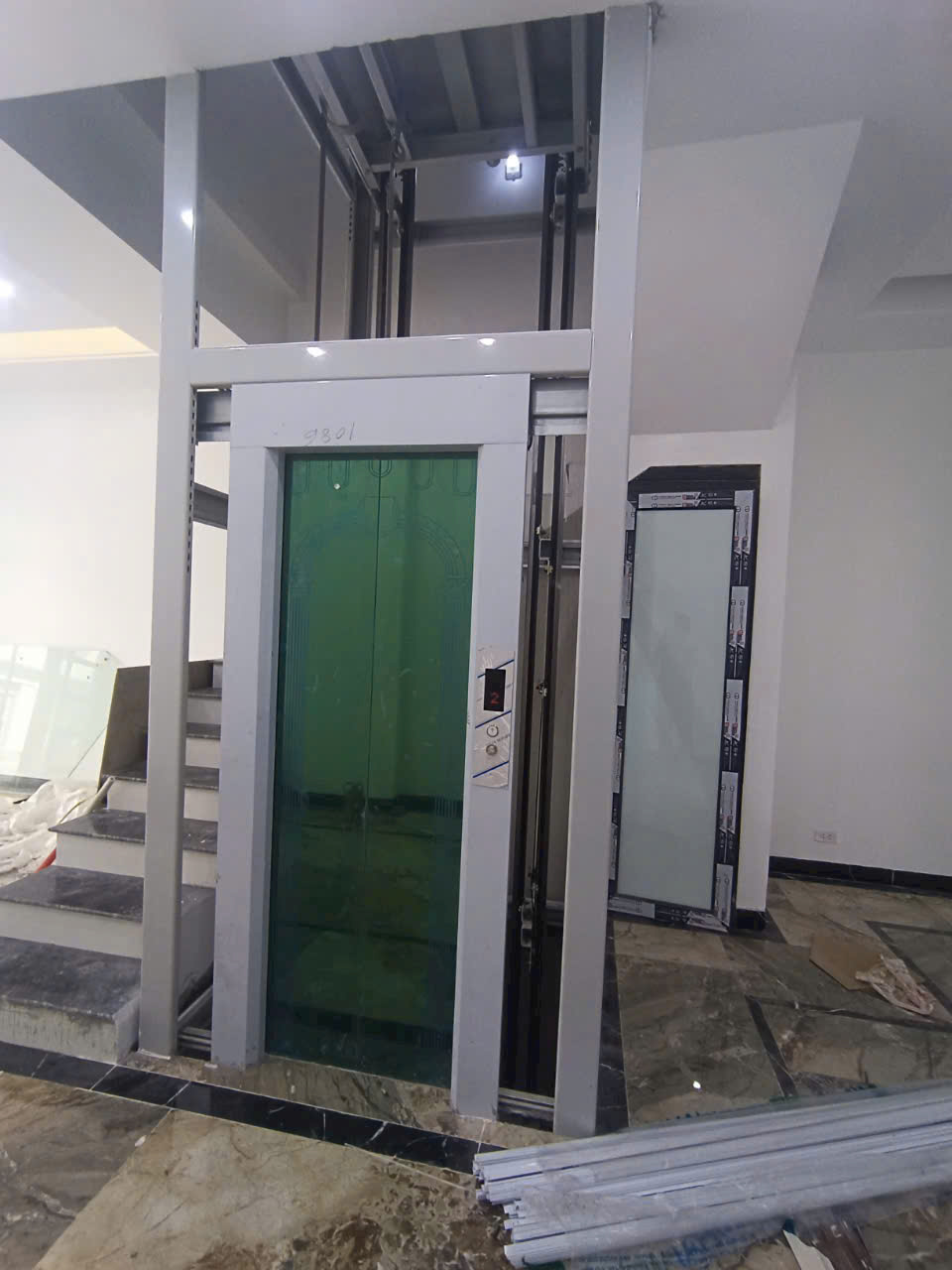 Thang máy gia đình cửa kính màu xanh đang lắp đặt trong nhà mới xây